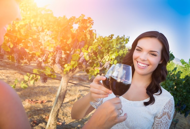 Uma bela jovem adulta a desfrutar de um copo de vinho a provar um brinde na vinha com amigos.