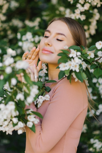 Uma bela jovem aproveita a vida em um jardim florescente de primavera contra o fundo de macieiras florescentes