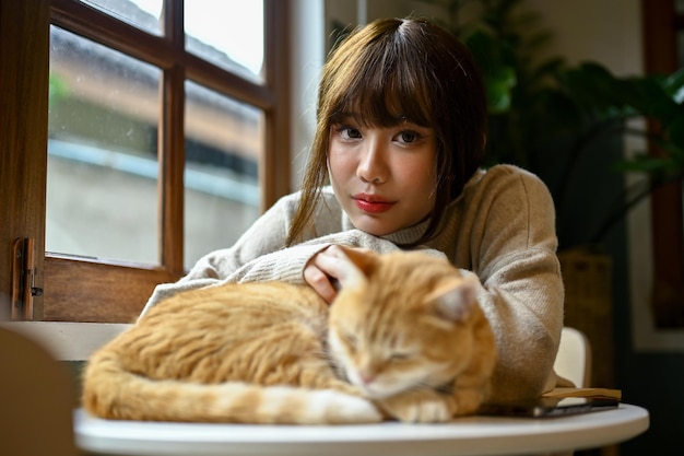 Uma bela jovem asiática descansando com seu gato em uma mesa em sua sala de estar