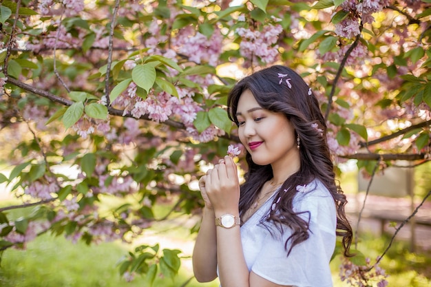 Uma bela jovem asiática em um vestido branco caminha em um parque florido. Sakura. Árvores florescendo. Primavera.