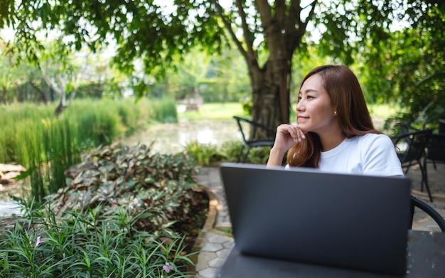 Uma bela jovem asiática faz uma pausa no trabalho no laptop no parque