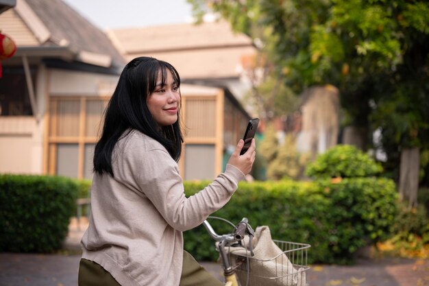 Uma bela jovem asiática feliz está usando seu smartphone enquanto anda de bicicleta na cidade