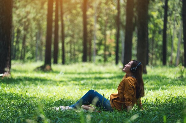 Uma bela jovem asiática gosta de ouvir música com fone de ouvido com sentimento feliz e relaxado no parque