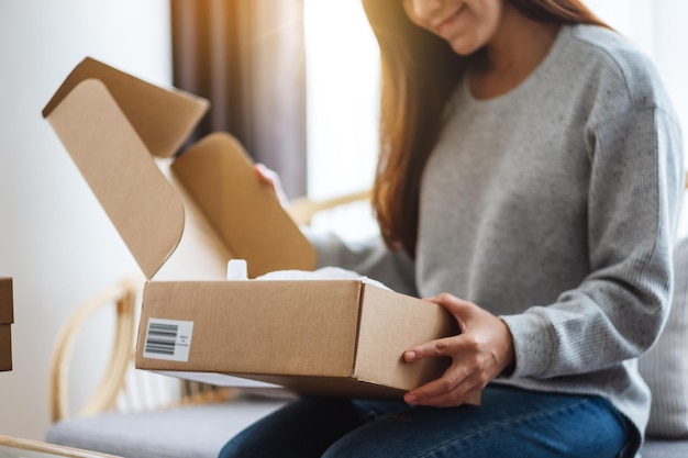 Foto uma bela jovem asiática recebendo e abrindo uma caixa postal em casa para entrega e conceito de compra online