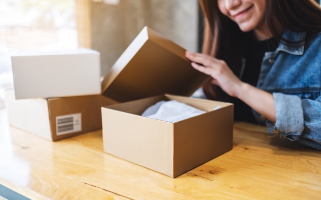 Foto uma bela jovem asiática recebendo e abrindo uma caixa postal em casa para entrega e conceito de compras on-line