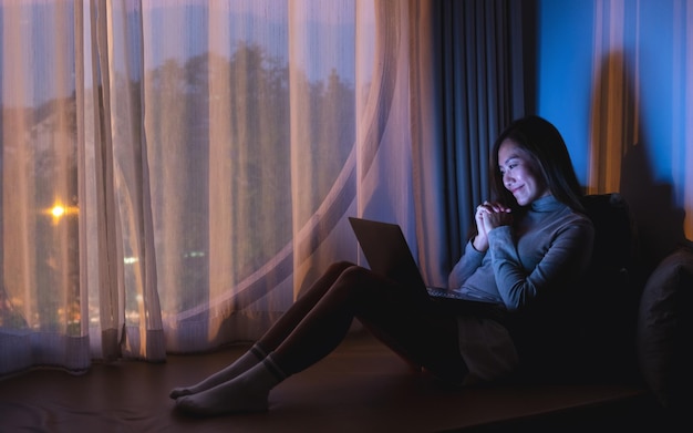 Uma bela jovem asiática usando laptop para videochamada com tela de luz brilhante na noite em casa
