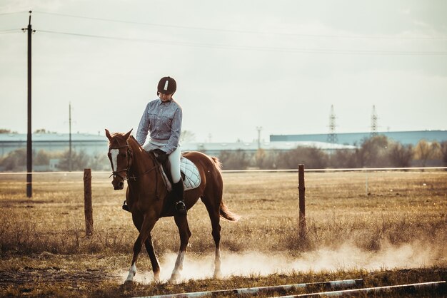 Uma bela jovem cavalgando um cavalo com um capacete preto e botas