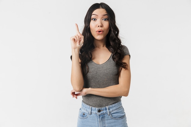 uma bela jovem chocada posando isolada sobre uma parede branca apontando para ter uma ideia.