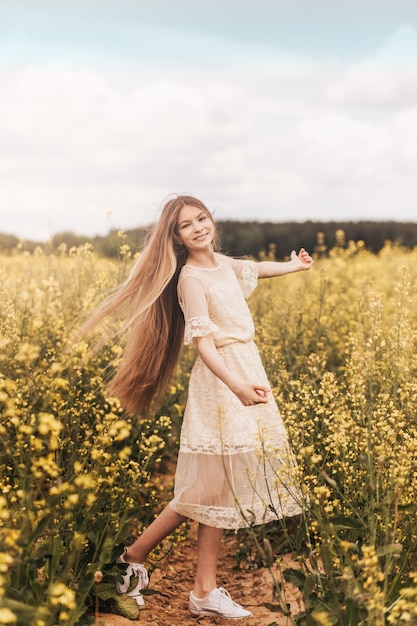 Uma bela jovem com cabelo comprido caminha em um campo de colza. Vertical