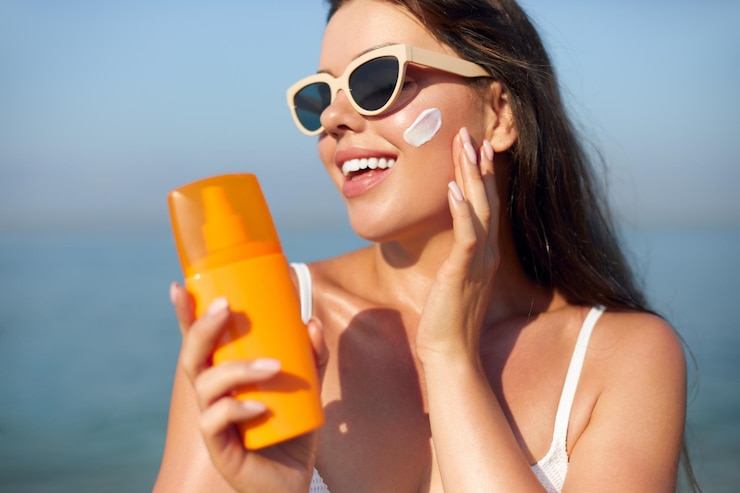 Foto uma bela jovem com creme solar no rosto, uma rapariga com uma garrafa de protetor solar na praia.