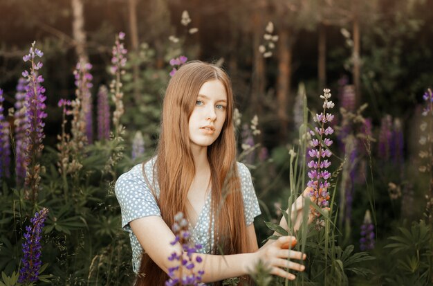 Uma bela jovem com longos cabelos vermelhos em uma clareira entre as flores. Tremoços
