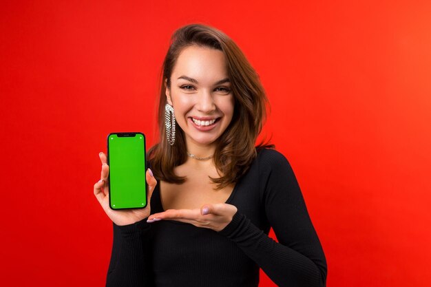 Uma bela jovem com maquiagem está segurando um celular com uma tela verde em um fundo vermelho Colocando anúncios em um smartphone