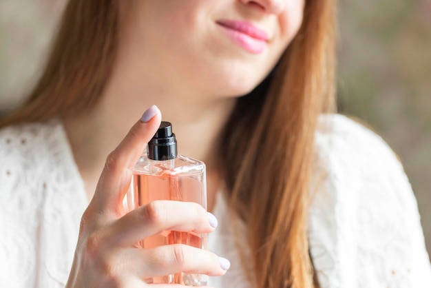 Uma bela jovem com uma garrafa de perfume a pulverizar no pescoço em casa.