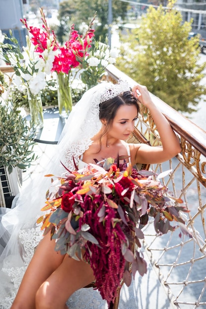 Uma bela jovem em lingerie requintada fica na varanda de um prédio de vários andares e tem um grande buquê de lindas flores nas mãos Manhã da noiva no dia do casamento