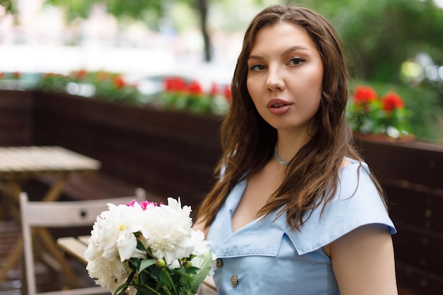 Uma bela jovem em um vestido azul com um buquê de peônias