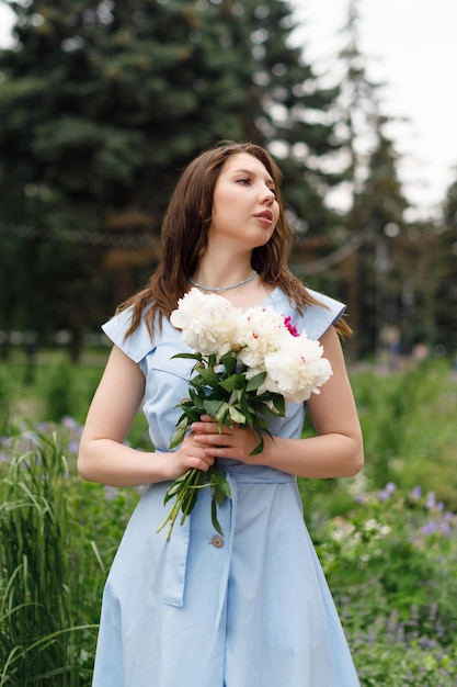 Uma bela jovem em um vestido azul com um buquê de peônias