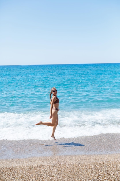 Uma bela jovem esguia em um maiô caminha ao longo da praia à beira-mar. conceito de férias de verão. foco seletivo