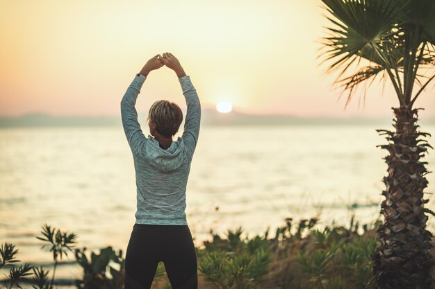 Uma bela jovem está fazendo exercícios de alongamento à beira-mar ao nascer do sol.