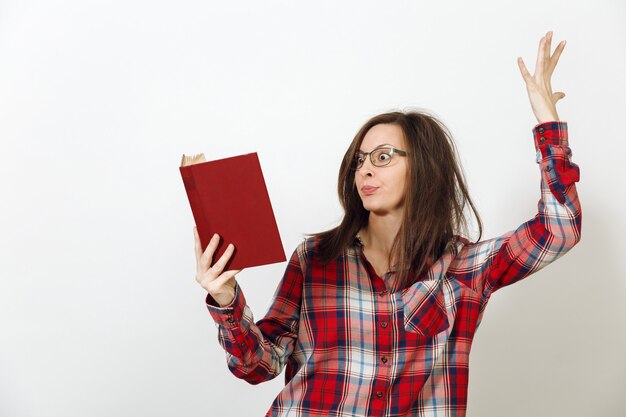 Uma bela jovem europeia de cabelos castanhos de óculos para visão com pele limpa e saudável, vestida com camisa xadrez vermelha casual, em pé com o livro sobre um fundo branco. conceito de leitura e estudo