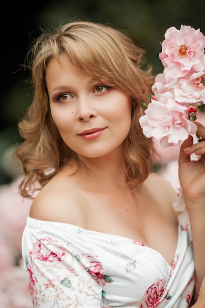 Uma bela jovem grávida está caminhando em um jardim de rosas. retrato de uma mulher grávida em um vestido. verão.