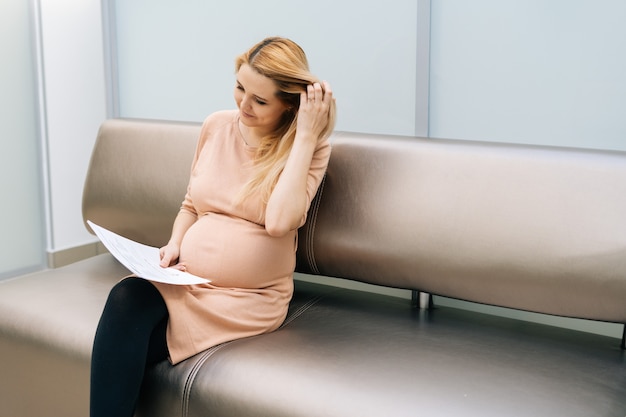 Uma bela jovem grávida sentada no corredor do hospital esperando para ver o ginecologista