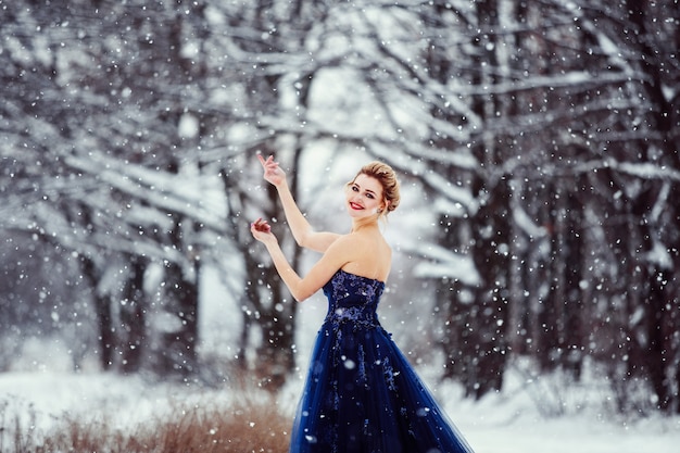 Uma bela jovem loira com um vestido azul exuberante posando em um parque de inverno nevado