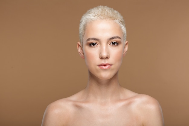 Uma bela jovem loira elegante com corte de cabelo curto posando isolado sobre a parede de parede bege escuro.