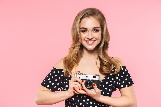 uma bela jovem posando isolada sobre uma parede rosa segurando uma câmera