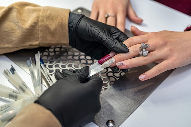 Uma bela jovem que trabalha em um salão de manicure oferece uma cor de esmalte para um de seus clientes e sorri O conceito do salão onde você faz manicure