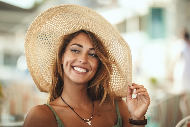 Uma bela jovem sorridente está andando pelas ruas de uma cidade mediterrânea e desfruta de um dia ensolarado de verão. Ela está posando com chapéu de palha e sorrindo.