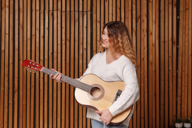 Uma bela jovem toca um violão clássico, no contexto de uma parede de madeira