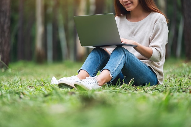 Uma bela jovem trabalhando e digitando no teclado do laptop enquanto está sentado no parque