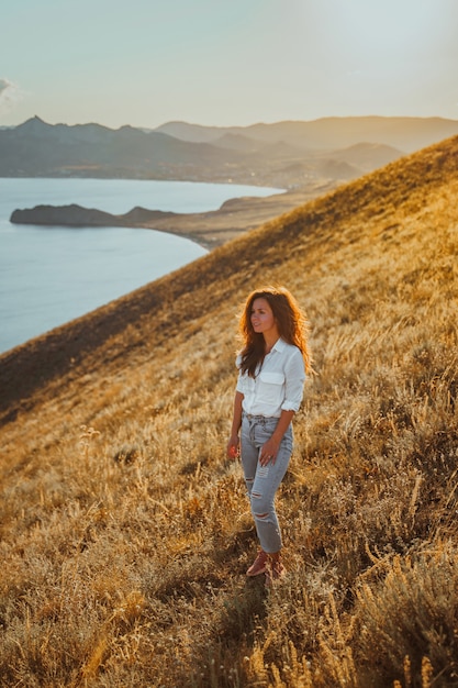 Uma bela jovem turista está sentada no topo de uma montanha e apreciando a vista do pôr do sol