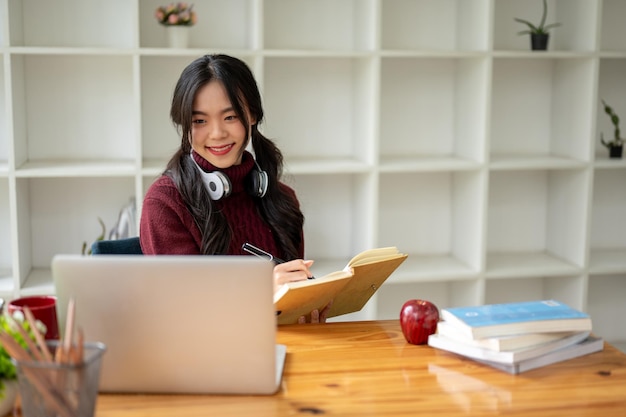 Uma bela jovem universitária asiática está fazendo lição de casa em seu laptop em uma mesa