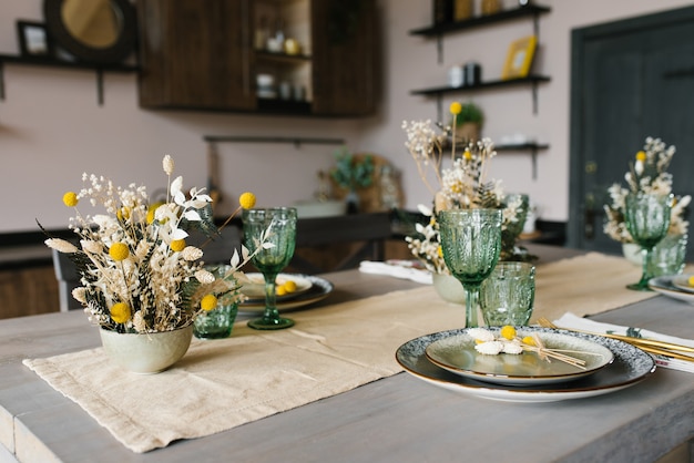 Uma bela mesa de jantar festiva em estilo rústico. Flores secas em um vaso de cerâmica na mesa