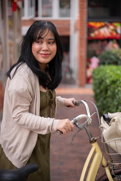 Uma bela mulher asiática positiva em um vestido bonito está andando e empurrando sua bicicleta na cidade