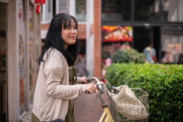 Uma bela mulher asiática positiva em um vestido bonito está andando e empurrando sua bicicleta na cidade