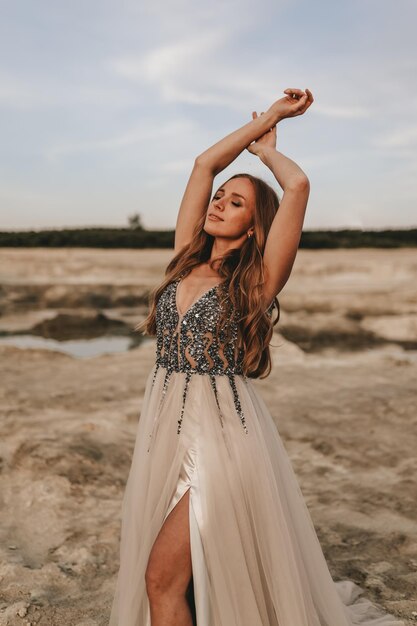 Foto uma bela mulher feliz em um vestido está relaxando dançando e se divertindo na areia do deserto