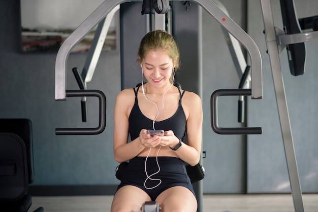 Uma bela mulher sorridente em fones de ouvido usando uma rede social e ouvindo música na academia, fitness e conceito de tecnologia