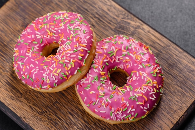 Uma bela rosquinha com esmalte rosa e polvilho colorido sobre um fundo escuro de concreto