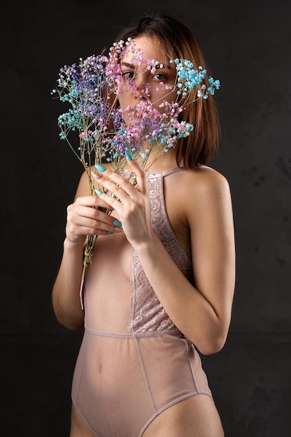 Uma bela senhora sexy em uma elegante roupa nua segura flores nas mãos retrato de beleza da moda da garota modelo de moda no estúdio