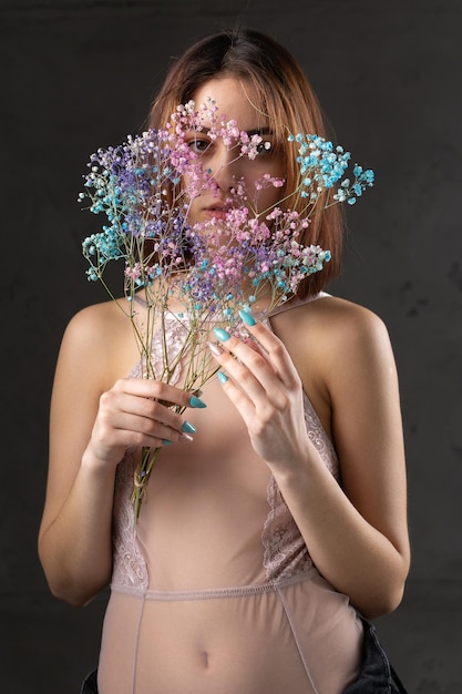 Uma bela senhora sexy em uma elegante roupa nua segura flores nas mãos Retrato de beleza da moda da garota modelo de moda no estúdio