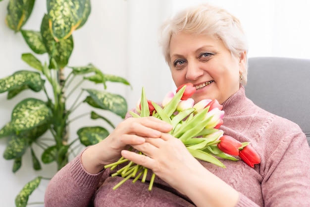 Uma bela velhinha cheirando um buquê de tulipas.