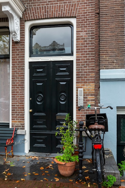 Uma bicicleta vermelha estacionada na entrada de uma típica casa de tijolos em Amsterdã em um dia chuvoso de outono. Vertical.