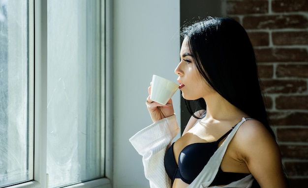 Uma boa bebida no café da manhã mulher adorável tomando café no café da manhã garota sensual desfrutando de sua bebida de café da manhã na janela receita de bebida de café da manhã para iniciar todas as manhãs