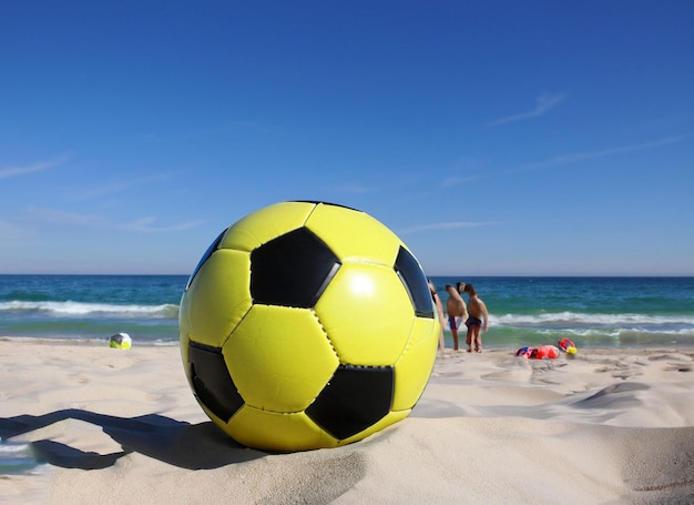 Foto uma bola de futebol amarela e preta fica na areia da praia.