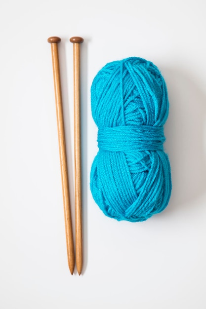 Uma bola de lã azul turquesa com agulhas de tricô de madeira