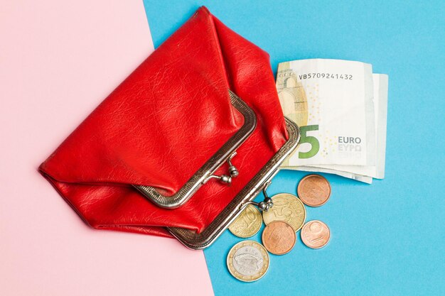 Uma bolsa vermelha com moedas e notas de euro em uma vista superior