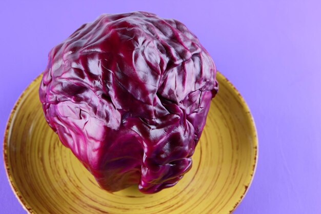 Uma cabeça inteira de repolho roxo em um prato amarelo em um fundo roxo Conceito de comida vegetariana Closeup