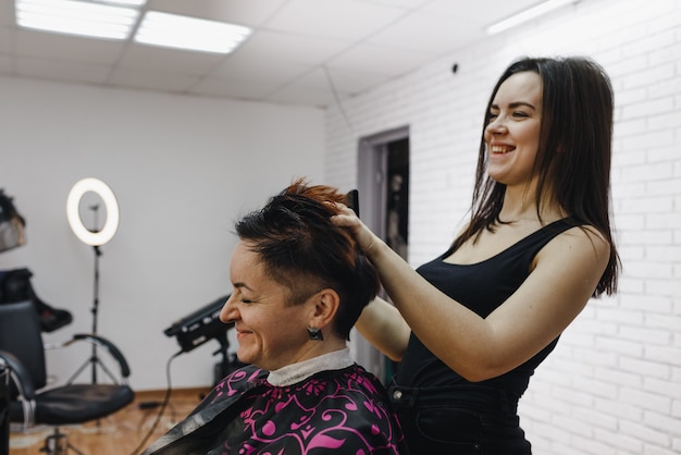 Foto uma cabeleireira faz o cabelo de uma cliente em um moderno salão de beleza e ri alegremente